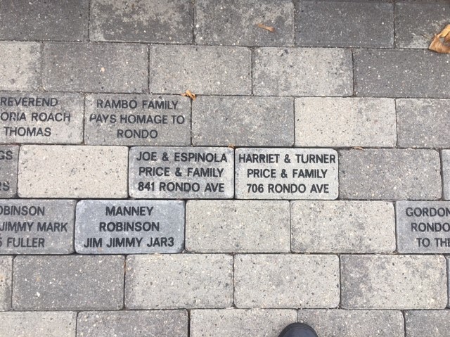 Concrete-colored bricks arranged as a sidewalk. At the center two bricks read: "JOE & ESPINOLA / PRICE & FAMILY / 841 RONDO AVE" and "HARRIET & TURNER / PRICE & FAMILY / 706 RONDO AVE."