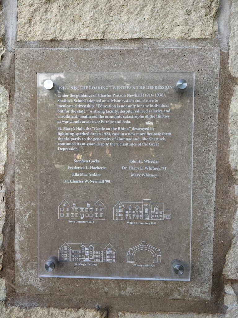 Glass plaque over a limestone pillar reads: "1917-1939: The Roaring Twenties & the Depression. Under the Guidance of Charles Watson Newhall (1916-1936), Shattuck School adopted an advisor system and strove to inculcate citizenship: 'Education is not only for the individual but for the state.' A strong faculty, despite reduced salaries and enrollmen, weathered the economic catastrophe of the thirties as war clouds rose over Europe and Asia."