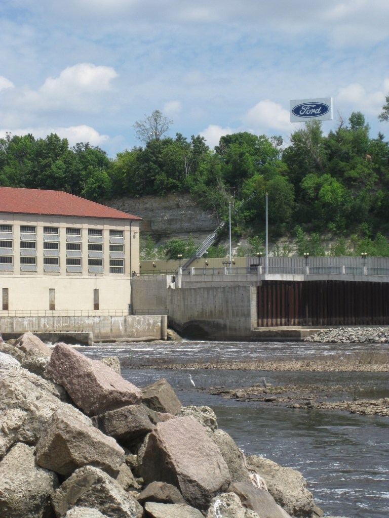 A lock and dam building on a river. In the background is a bluff with green trees.